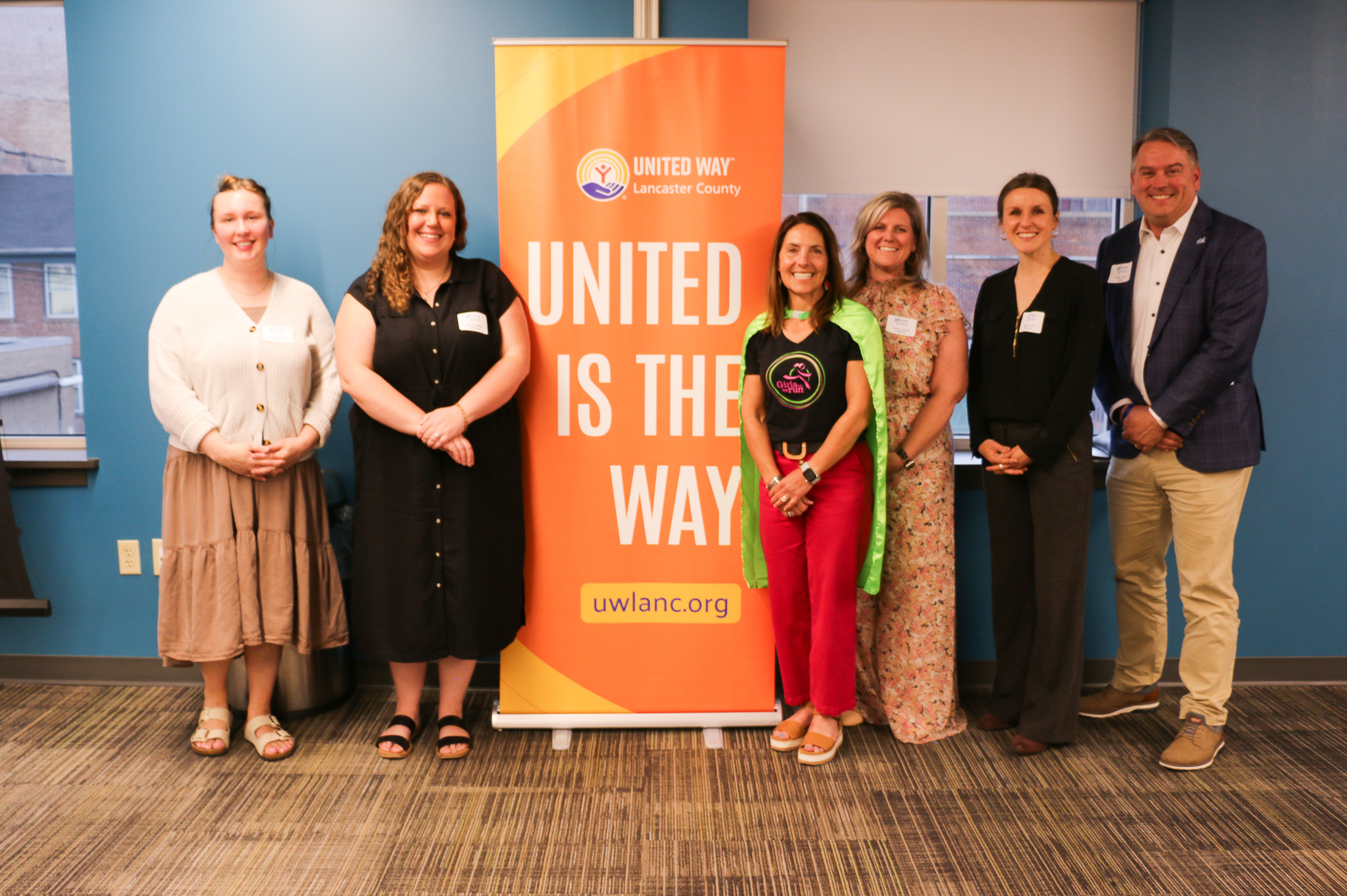 5 women and 1 man in front of a United Is The Way sign